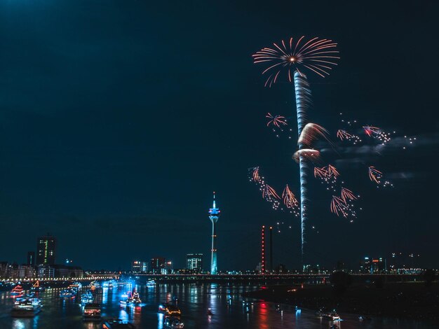 Firework display over river in city against clear sky at night