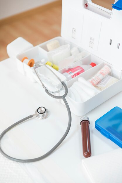 Photo first aid kit box with stethoscope and blood sample tube on table