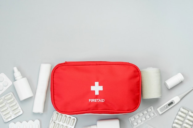 First aid kit red bag with medical equipment and medications for emergency treatment. Top view flat lay on gray background. Copy space.