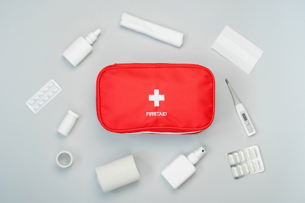 First aid kit red bag with medical equipment and medications for emergency treatment. Top view flat lay on gray background.
