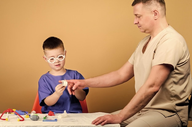 First aid Medical help Trauma and injurie Medicine concept Kid little doctor sit table medical tools Health care Medical examination Boy cute child and his father doctor Hospital worker