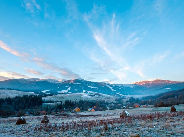 First autumn frosts on pasture with haystacks and sunrise in the mountains village