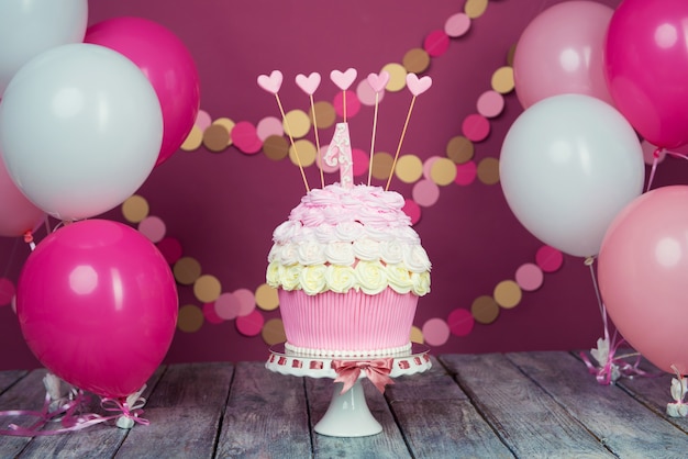 Foto prima torta di compleanno con unità su sfondo rosa con palline e ghirlanda di carta.