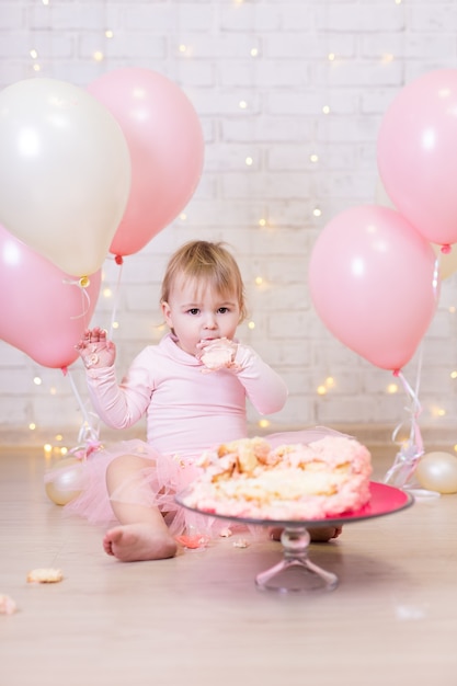 Prima festa di compleanno bambina divertente che mangia e rompe la torta sullo sfondo del muro di mattoni
