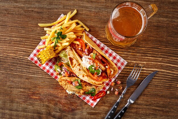 First corn tortilla with grilled chicken fillet second with fish fillet sauce and beer on wooden tab...