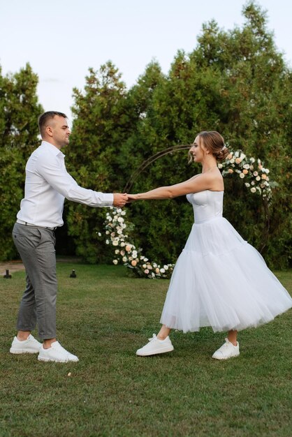 The first dance of the groom and bride in a short wedding dress on a green meadow