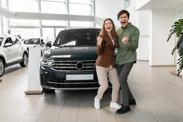 First family car happy young caucasian couple shaking fists making yes gesture after buying new auto