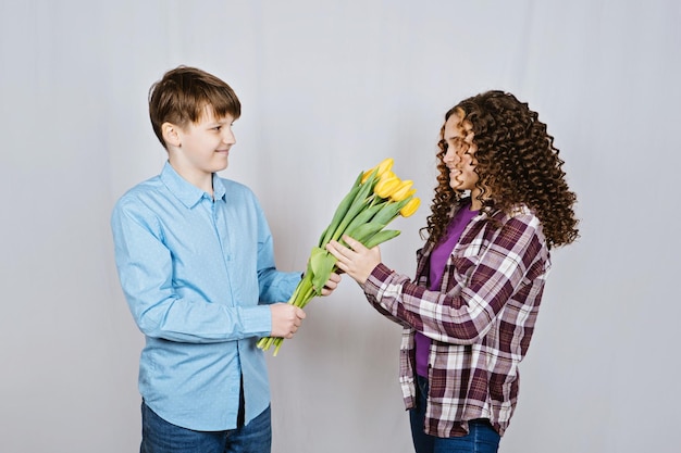 最初の愛の概念の 10 代の少年は彼のガール フレンドに白い背景に黄色のチューリップの花束を与える