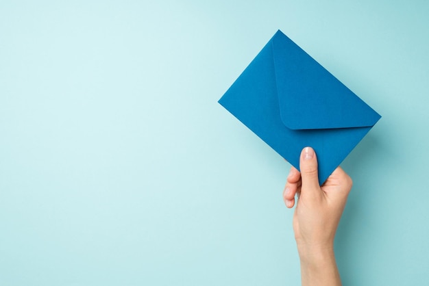 Photo first person top view photo of hand holding closed blue envelope on isolated pastel blue background with copyspace