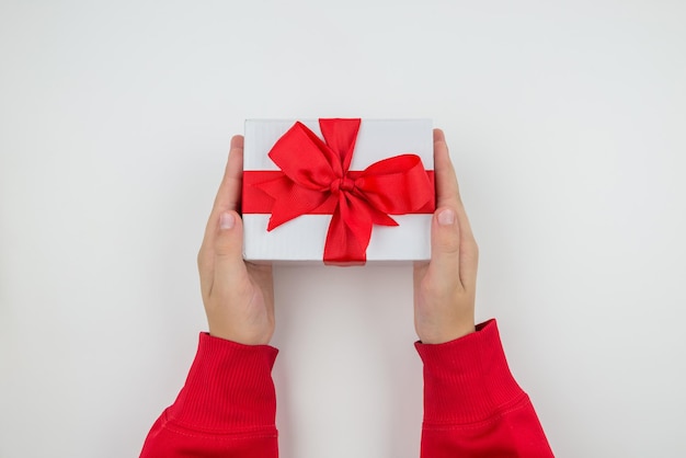 First person top view of young woman's hands holding white gift
box with red ribbon on isolated white background