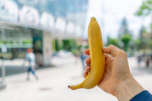 First person view of hand hold fresh ripe banana, meal or snack in the city streets