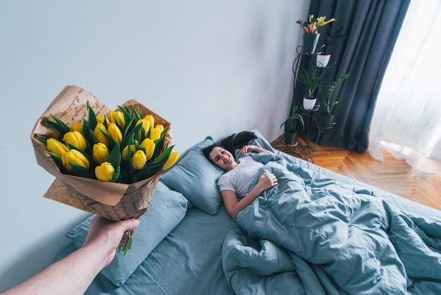 First person view man brengt bloemen naar bed voor een romantisch verrassingsconcept voor slapende vriendin