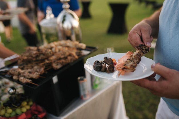 First person view of somebody hold plate and take some snack on plate Outdoor party