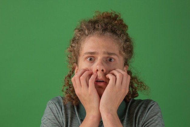 Photo the first signs of coronavirus headache in a man the guy holds his head with an emotion of fear on his face curly guy on a green background looking at the camera