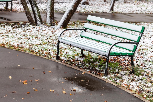The first snow on wooden bench in city park