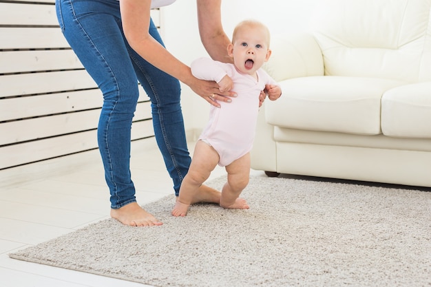 First steps of baby toddler learning to walk in white sunny living room. Footwear for child.