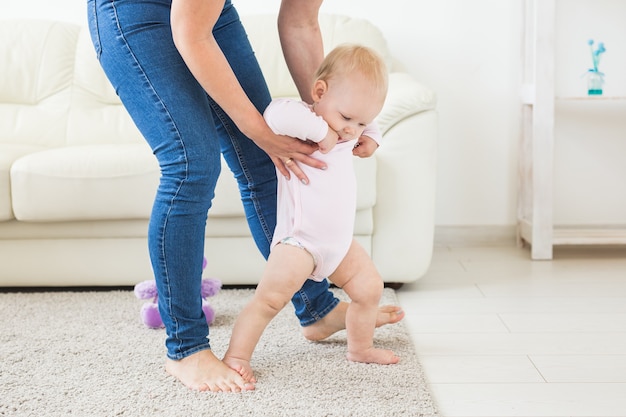 Photo first steps of baby toddler learning to walk in white sunny living room. footwear for child.