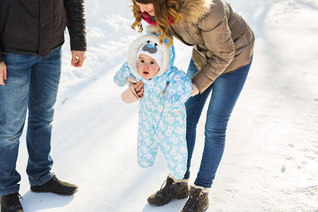 첫 번째 단계입니다. 걷는 법을 배우는 작은 아기. 겨울 공원에서 유아 소년과 어머니와 아버지