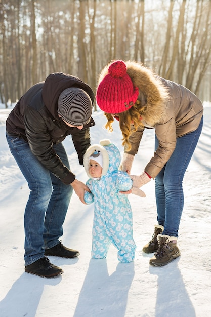 First steps. Little baby learning to walk. Mother and father with toddler boy at the winter park