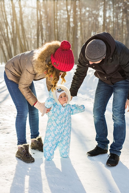 最初のステップ。歩くことを学ぶ小さな赤ちゃん。冬の公園で幼児の男の子と母と父