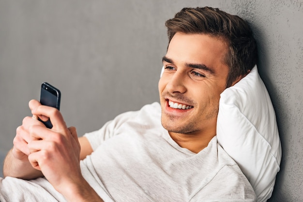 First thing you do after awakening. Cheerful young man holding smartphone