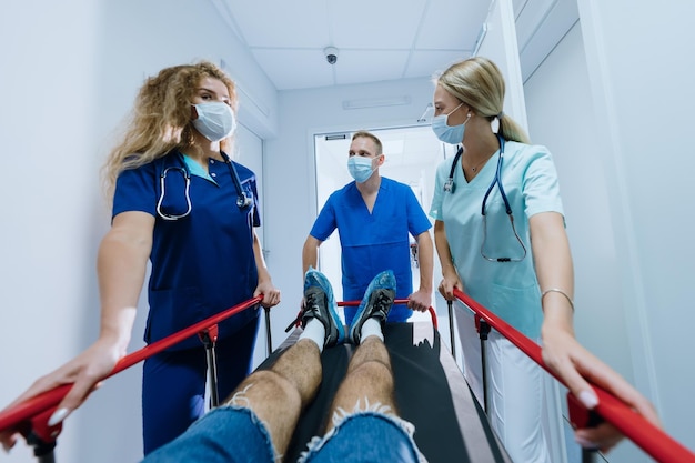 Firstperson viewA professional team of paramedics is rolling a gurney with a patient along the corridor of the hospital Selective focus on male doctor