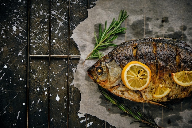 Fish baked in oven with lemon and rosemary on parchment paper laid out on grate dark background