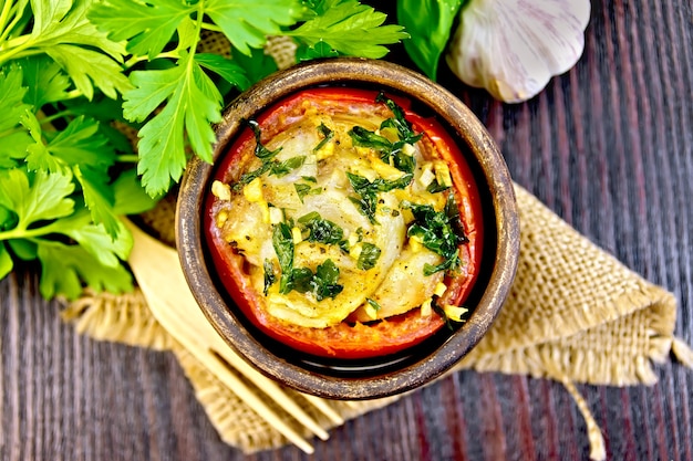 Fish baked in tomato in Zandvoort in clay bowl on a napkin of burlap, parsley on a dark wooden board on top