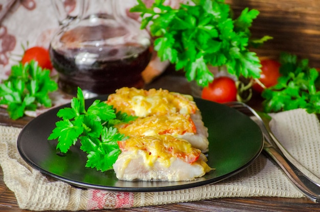 写真 暗い背景にホワイトソースで野菜とチーズを添えて焼いた魚