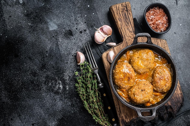 Fish balls with tuna in tomato sauce in a pan. Black background. Top view. Copy space.