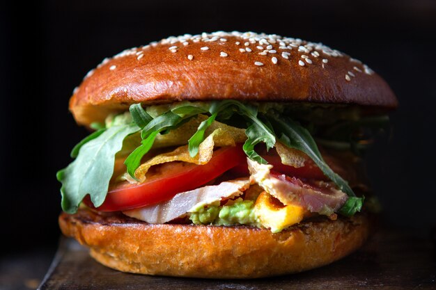 Fish Burger with fresh tuna, guacamole sauce and arugula on dark background