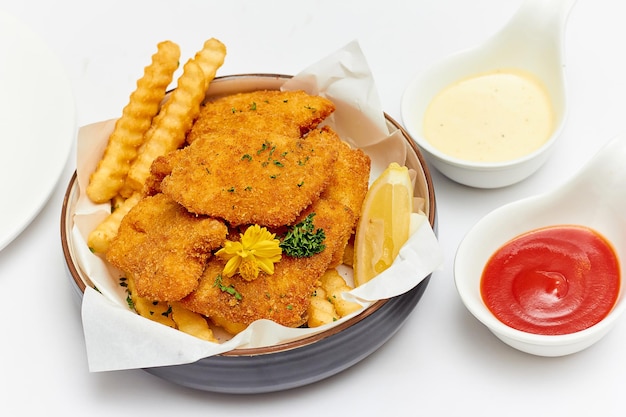 피쉬 앤 칩스(Fish and Chips)는 꽃과 파슬리, 디핑 소스 케첩, 마요네즈로 장식된 큰 그릇에 반죽된 생선과 감자 튀김 감자를 흰색 배경에 분리했습니다.