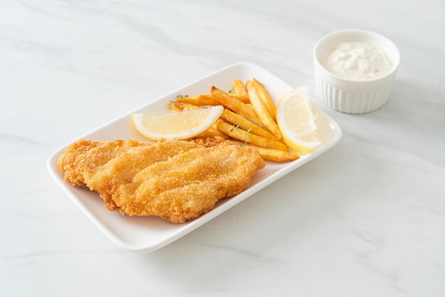 рыба с жареным картофелем - жареное филе рыбы с картофельными чипсами и лимоном на белой тарелке