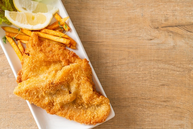 Fish and chips - fried fish fillet with potatoes chips and lemon on white plate