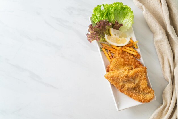 fish and chips - fried fish fillet with potatoes chips and lemon on white plate