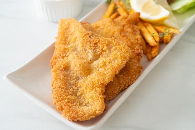 fish and chips - fried fish fillet with potatoes chips and lemon on white plate