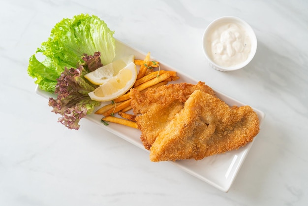 fish and chips - fried fish fillet with potatoes chips and lemon on white plate