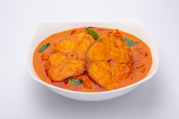 Fish curry_Seer fish curry, традиционное индийское рыбное карри, специальное блюдо из Кералы, расположенное в белой миске, украшенное листьями карри на белом фоне