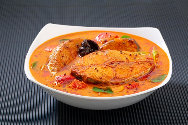 Fish curry_seer fish curry ,traditional indian fish curry\
,kerala special dish using coconut ,arranged in a white bowl\
garnished with curry leaves and malabar tamarind on white textured\
background