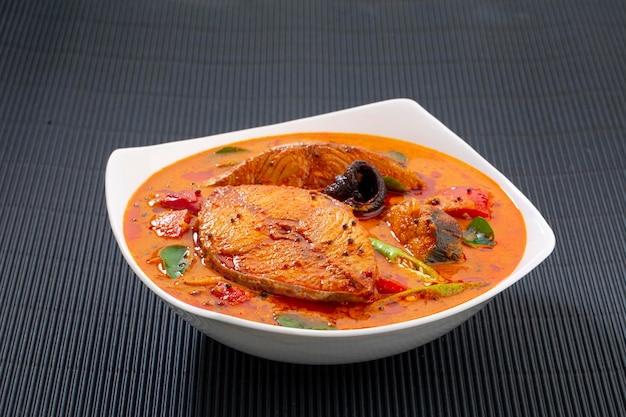 Fish curry_Seer рыбное карри, традиционное индийское рыбное карри, специальное блюдо из Кералы с использованием кокоса, расположенное в белой миске, украшенное листьями карри и малабарским тамариндом на белом текстурированном фоне