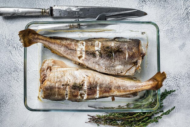 写真 魚料理-焼きタラの魚をハーブと一緒に焼き皿に入れます。白色の背景。上面図。