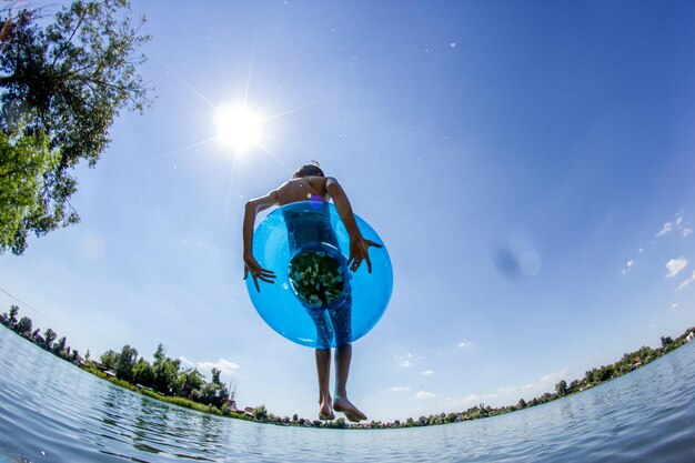 Fish-eye lens view of boy jumping with inflatable ring in lake