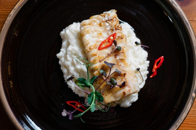 Fish fillet baked with rice on a black plate closeup