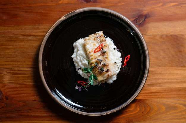 Филе рыбы, запеченное с рисом на черной тарелке