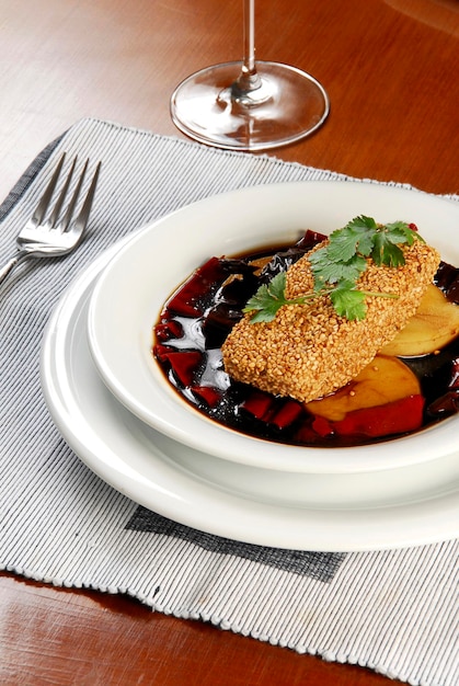 fish fillet covered with sesame in an apple sauce on a wooden table with a fork and tablecloth