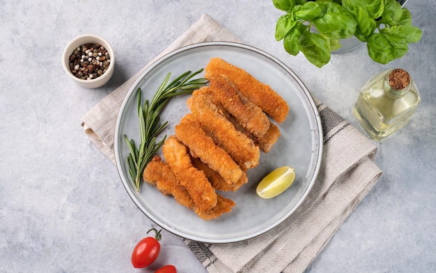 Fish fillet sticks fried on a plate with rosemary on a light background with tomatoes and spices Dietary and healthy food Top view