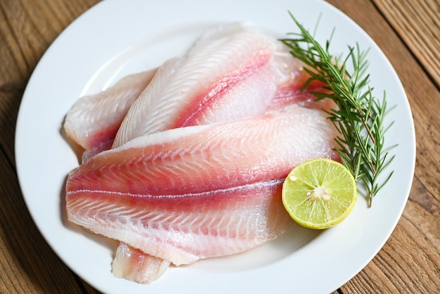 fish fillet on white plate with ingredients for cooking, fresh raw pangasius fish fillet with herb and spices lemon lime and rosemary, meat dolly fish tilapia striped catfish