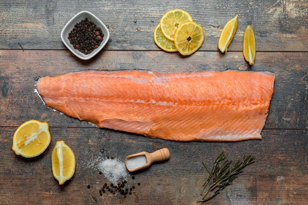 Photo fish fillet with culinary ingredients salt herbs pepper and lemon raw atlantic salmon fillet on skin on dark wooden board during cooking