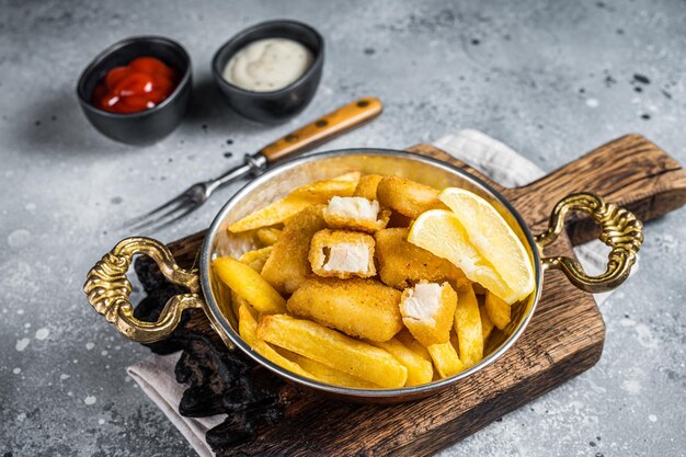 Fish fingers and Chips british fast food with tartar and tomato sauce seafood sticks Gray background Top view