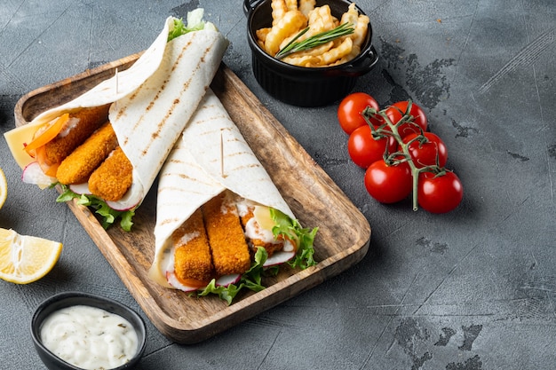 Fish fingers roll and tartar sauce set, on wooden tray, on gray table